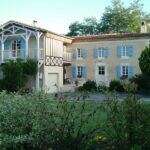 Maison avec volets bleus et balcon blanc.