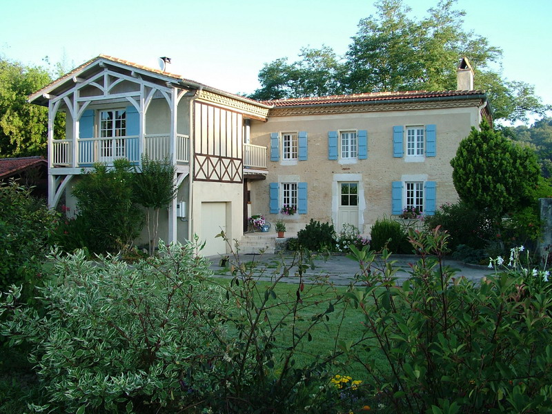 Maison avec volets bleus et balcon blanc.