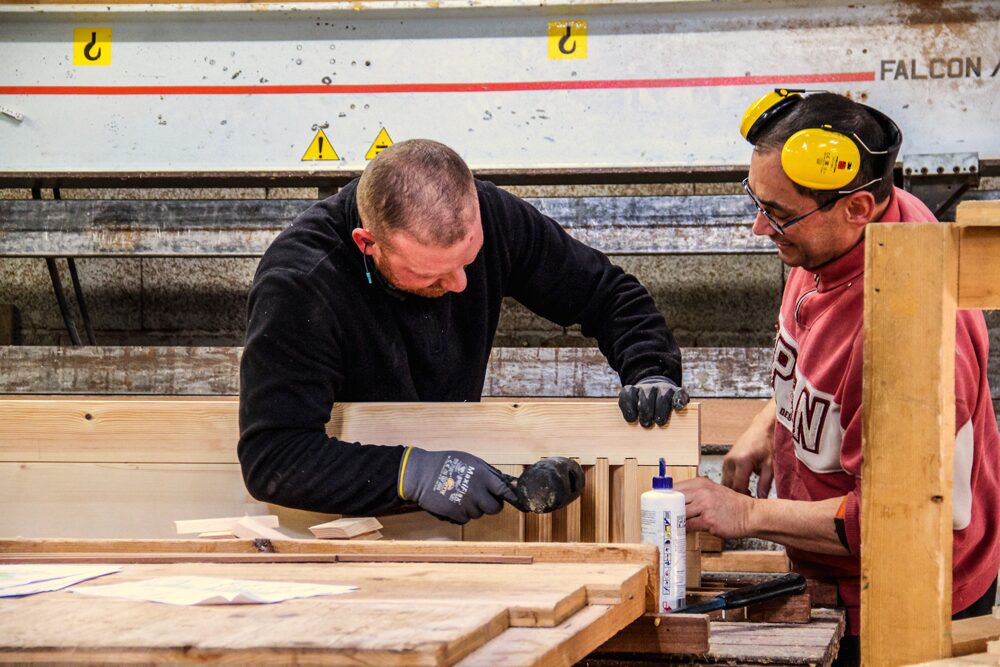 Deux artisans travaillant sur des volets Guignard en atelier.
